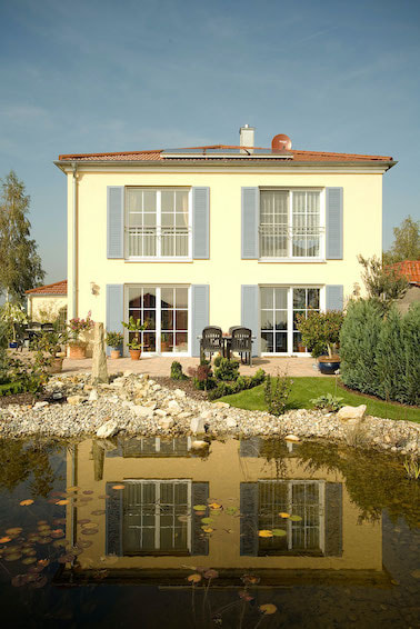 Kunststofffenster zieren die Fassade eines Hauses mit Gartenanlage und Teich